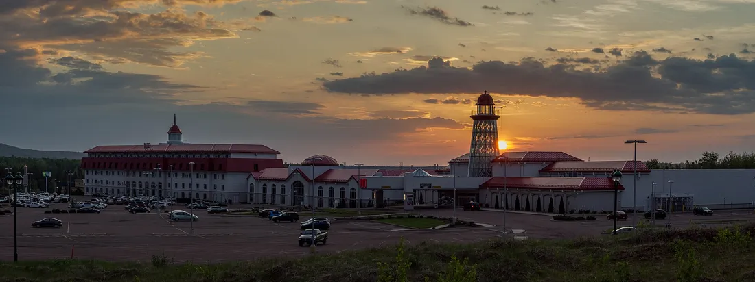 Photograph: the hotel block, red-roofed casino wings and the lighthouse-style tower of Casino New Brunswick at sunset, seen across its parking lot.